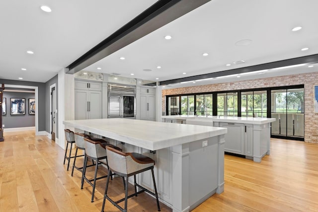 kitchen featuring a breakfast bar area, a spacious island, stainless steel built in refrigerator, light stone countertops, and light hardwood / wood-style floors