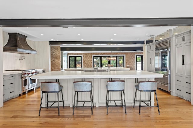 kitchen with a breakfast bar area, premium appliances, custom exhaust hood, a large island, and light hardwood / wood-style floors