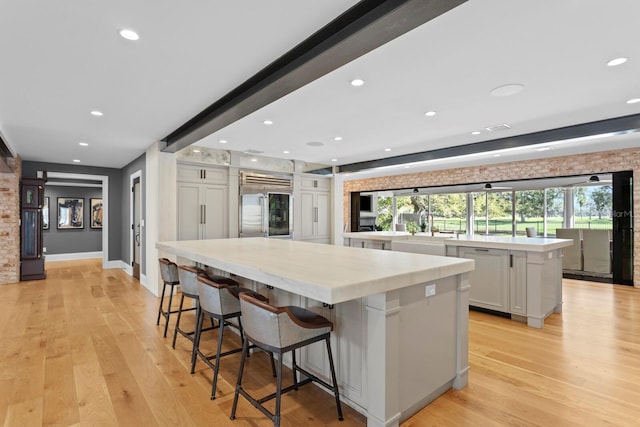 kitchen featuring a spacious island, stainless steel built in refrigerator, a breakfast bar area, white cabinetry, and light hardwood / wood-style flooring