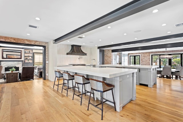 kitchen with white cabinetry, beam ceiling, a spacious island, a kitchen bar, and light wood-type flooring