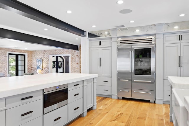 kitchen with built in appliances, white cabinets, and light wood-type flooring