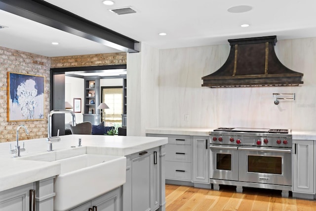 kitchen featuring gray cabinets, sink, double oven range, custom range hood, and light hardwood / wood-style flooring