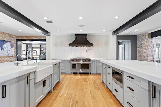 kitchen featuring sink, stainless steel appliances, light hardwood / wood-style floors, light stone countertops, and custom exhaust hood