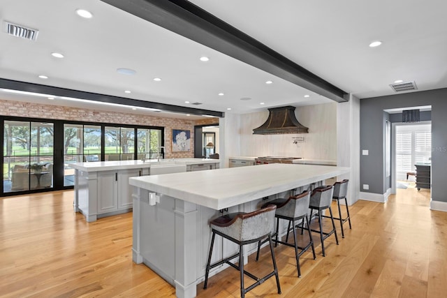 kitchen with a spacious island, a kitchen bar, white cabinetry, light wood-type flooring, and kitchen peninsula