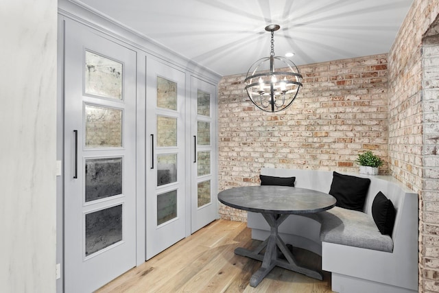 dining room featuring breakfast area, light hardwood / wood-style flooring, a chandelier, and brick wall