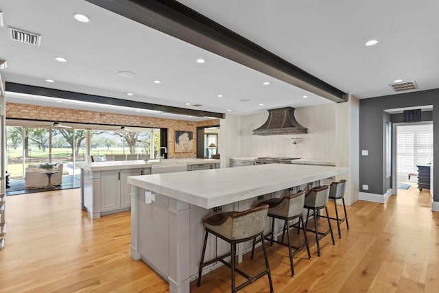 kitchen featuring light hardwood / wood-style flooring, a breakfast bar, white cabinetry, a spacious island, and custom range hood