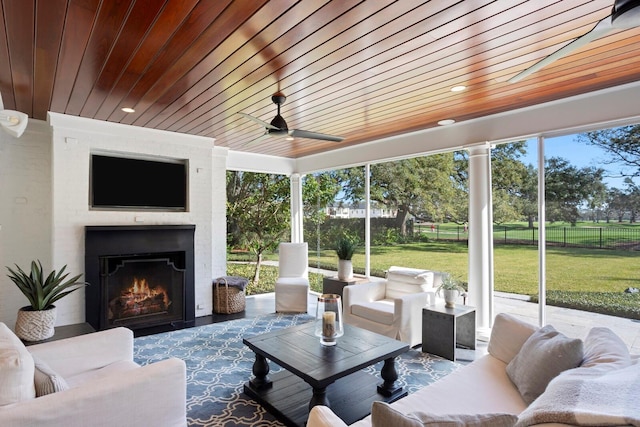 sunroom featuring a fireplace, wooden ceiling, ceiling fan, and plenty of natural light