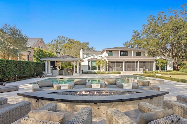 rear view of property with a gazebo, a swimming pool with hot tub, exterior bar, a fire pit, and a sunroom