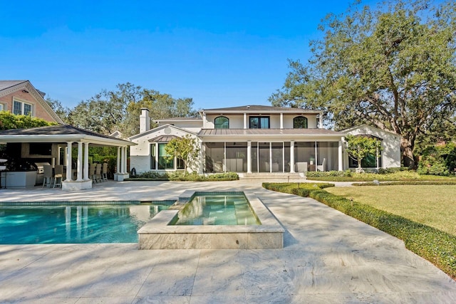 rear view of house with a lawn, a pool with hot tub, a gazebo, a sunroom, and a patio area