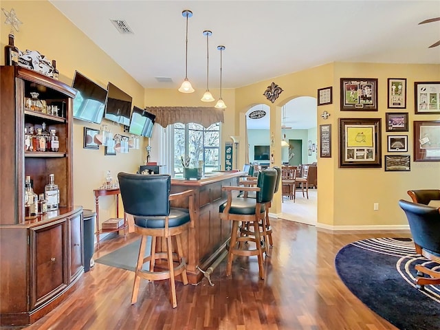 bar featuring a dry bar, visible vents, ceiling fan, wood finished floors, and decorative light fixtures