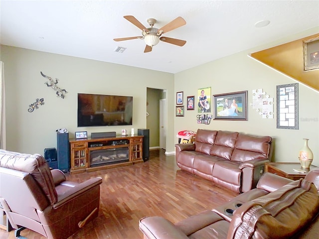 living area with wood finished floors, visible vents, baseboards, a ceiling fan, and a glass covered fireplace