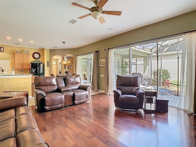 living room featuring a ceiling fan, arched walkways, visible vents, and wood finished floors