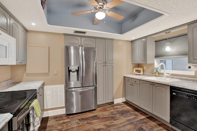 kitchen featuring appliances with stainless steel finishes, sink, gray cabinets, dark hardwood / wood-style floors, and a raised ceiling