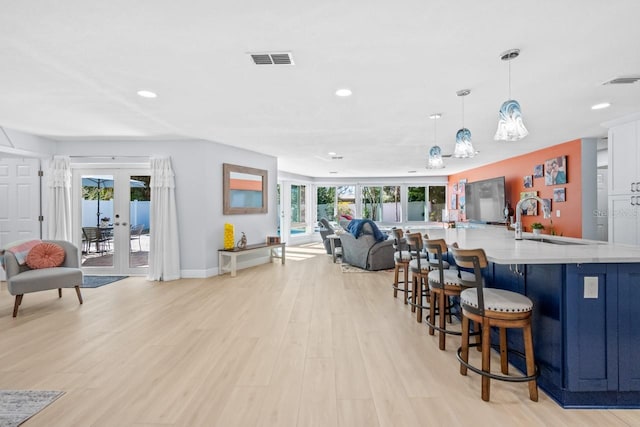 kitchen with light hardwood / wood-style flooring, a kitchen breakfast bar, french doors, decorative light fixtures, and sink