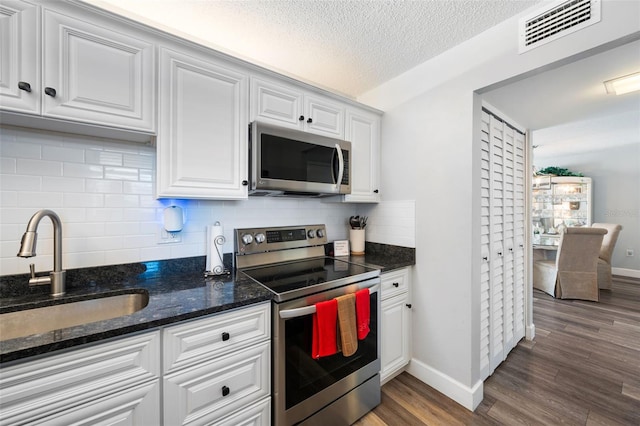 kitchen with visible vents, white cabinets, appliances with stainless steel finishes, wood finished floors, and a sink