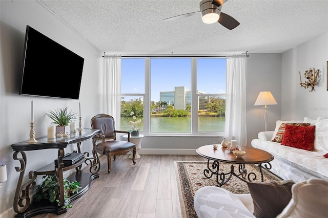 living area with a textured ceiling, ceiling fan, a water view, baseboards, and light wood finished floors