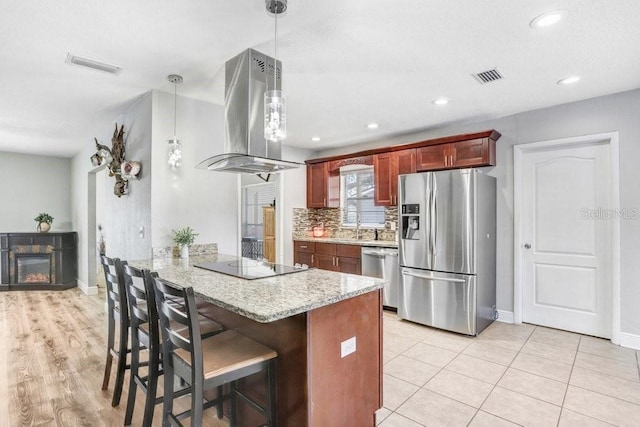 kitchen featuring visible vents, island range hood, a glass covered fireplace, a peninsula, and stainless steel appliances