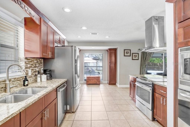 kitchen with tasteful backsplash, appliances with stainless steel finishes, light stone counters, island exhaust hood, and a sink