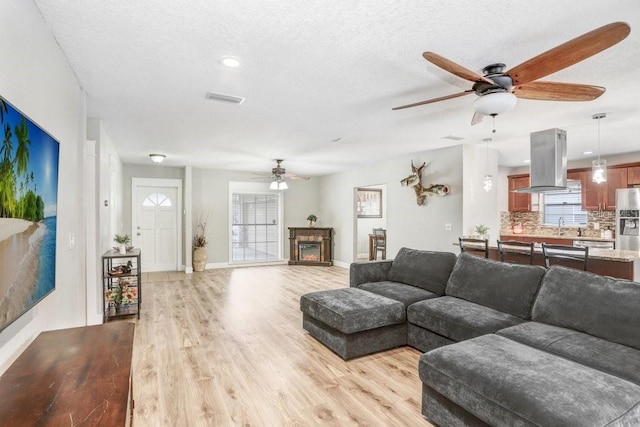 living room featuring a textured ceiling, light wood-style flooring, visible vents, baseboards, and a lit fireplace