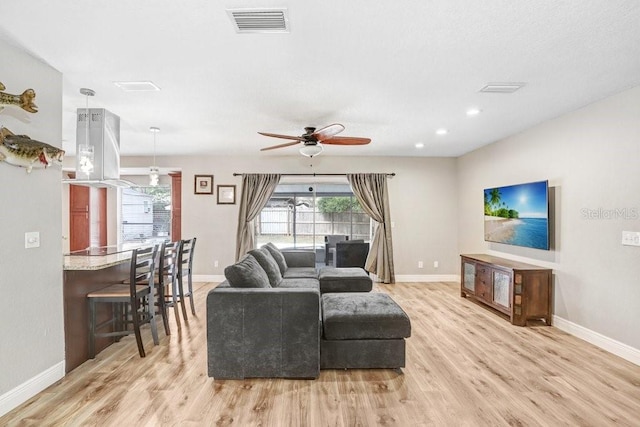 living area featuring a ceiling fan, light wood-type flooring, visible vents, and baseboards