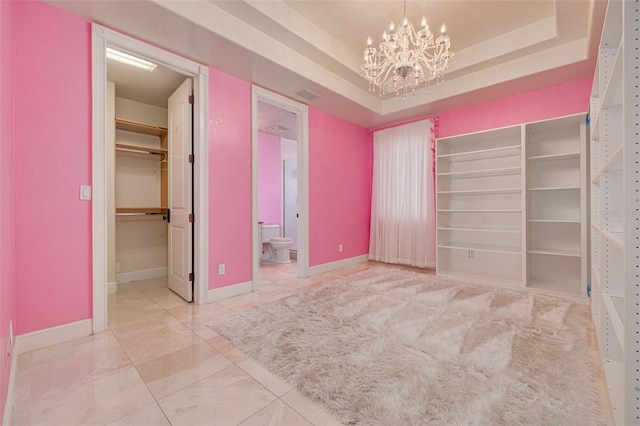 unfurnished bedroom with ensuite bathroom, a spacious closet, a notable chandelier, a raised ceiling, and a closet