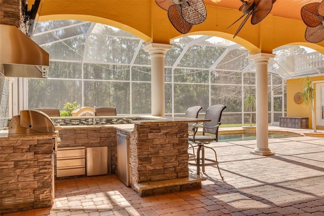 view of patio with glass enclosure, an outdoor bar, ceiling fan, and exterior kitchen