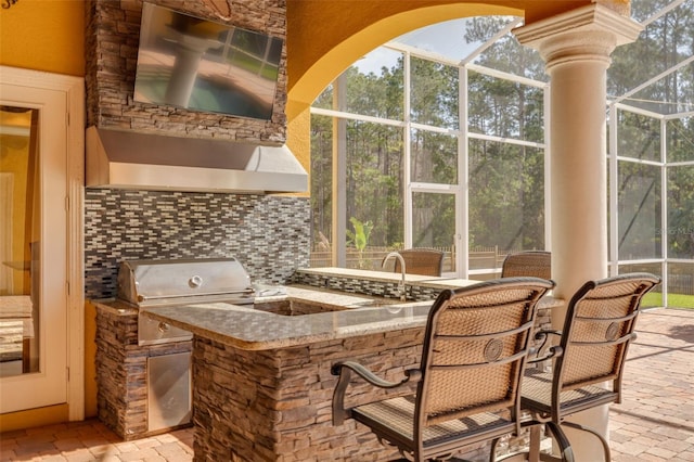 view of patio with exterior kitchen, area for grilling, a wet bar, and glass enclosure