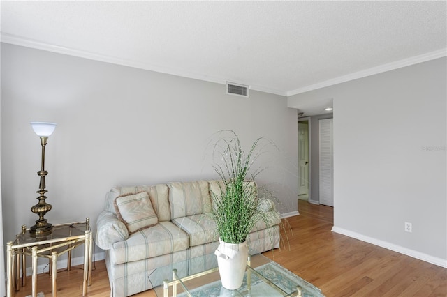 living room featuring baseboards, visible vents, ornamental molding, wood finished floors, and a textured ceiling