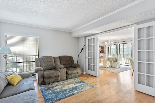 living area with french doors, an inviting chandelier, ornamental molding, a textured ceiling, and wood finished floors