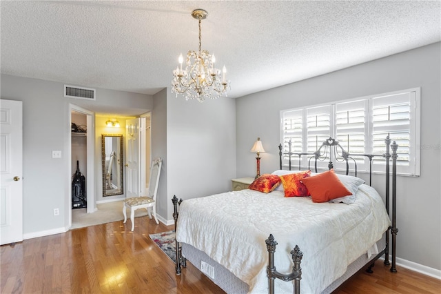 bedroom featuring visible vents, a textured ceiling, baseboards, and wood finished floors