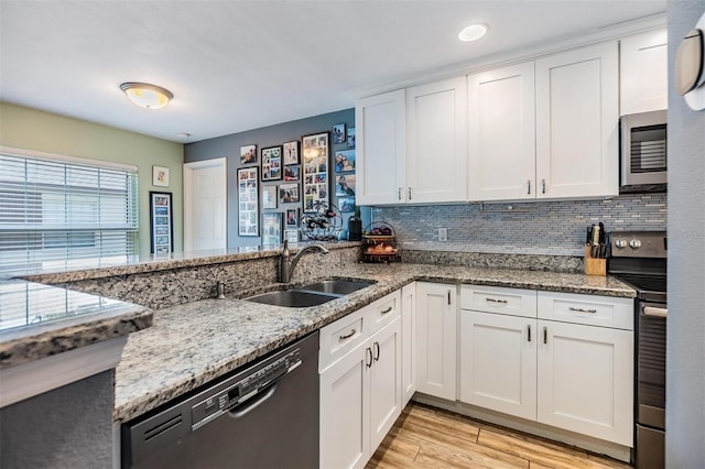 kitchen featuring appliances with stainless steel finishes, stone countertops, white cabinetry, sink, and light hardwood / wood-style flooring