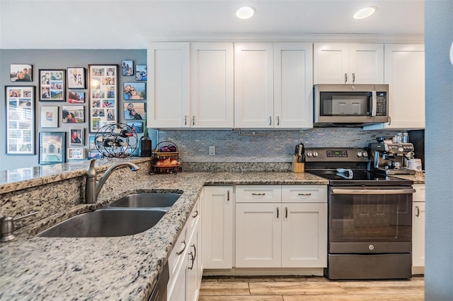 kitchen with sink, light stone counters, tasteful backsplash, appliances with stainless steel finishes, and white cabinets