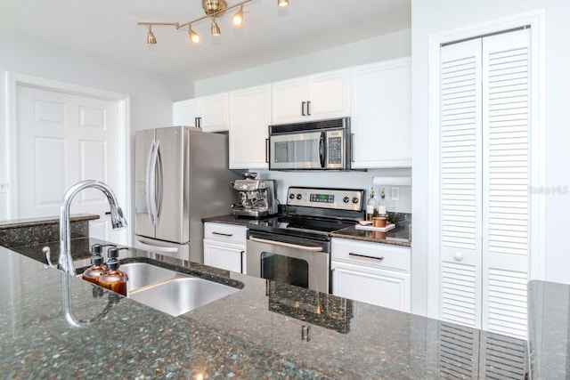 kitchen with appliances with stainless steel finishes, white cabinets, a sink, and dark stone counters