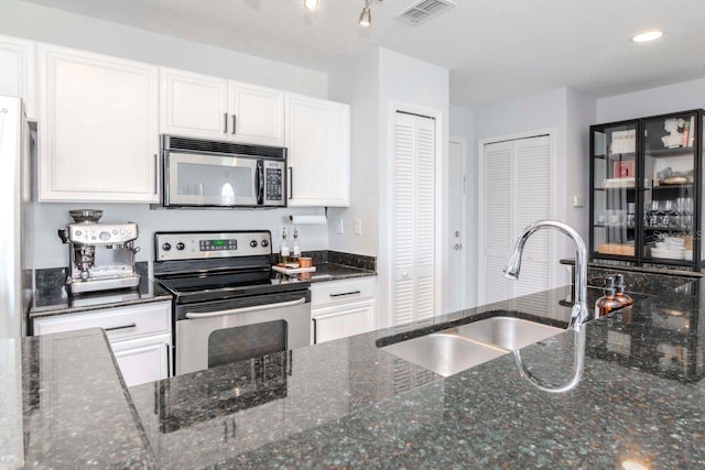 kitchen featuring visible vents, appliances with stainless steel finishes, white cabinetry, a sink, and dark stone counters