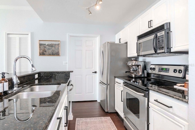 kitchen with stainless steel appliances, dark stone countertops, a sink, and white cabinetry