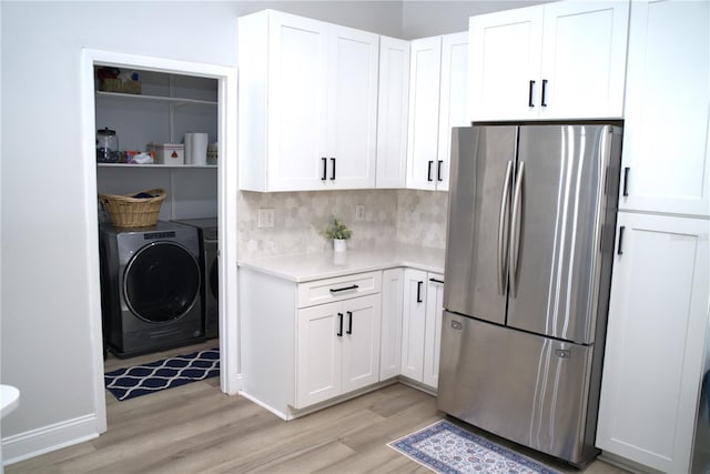 kitchen with white cabinetry, stainless steel fridge, washer and dryer, and light hardwood / wood-style flooring