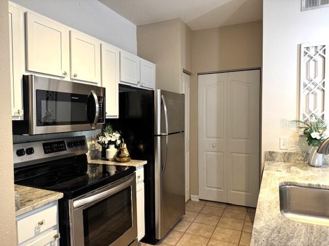 kitchen featuring light tile patterned floors, sink, appliances with stainless steel finishes, white cabinetry, and light stone countertops