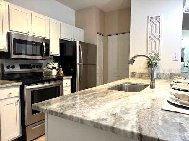 kitchen featuring appliances with stainless steel finishes, sink, white cabinets, kitchen peninsula, and light stone countertops