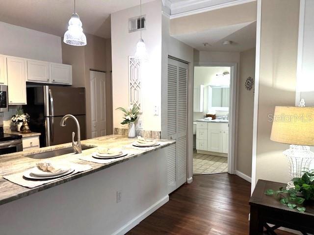 kitchen featuring pendant lighting, sink, white cabinets, light stone counters, and stainless steel appliances