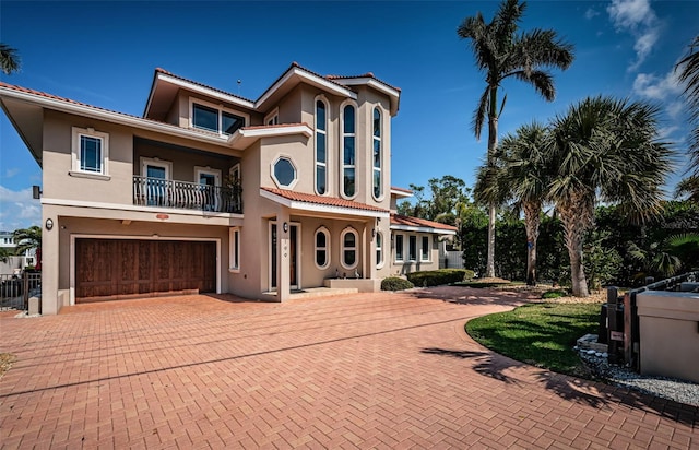 mediterranean / spanish house with a garage, decorative driveway, a balcony, and stucco siding