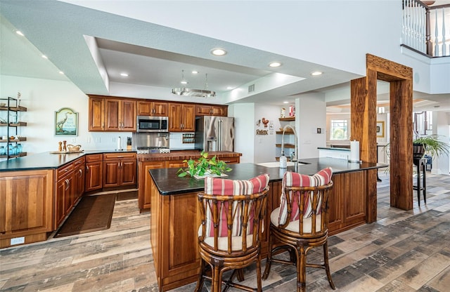 kitchen featuring stainless steel appliances, dark countertops, dark wood finished floors, and a center island with sink