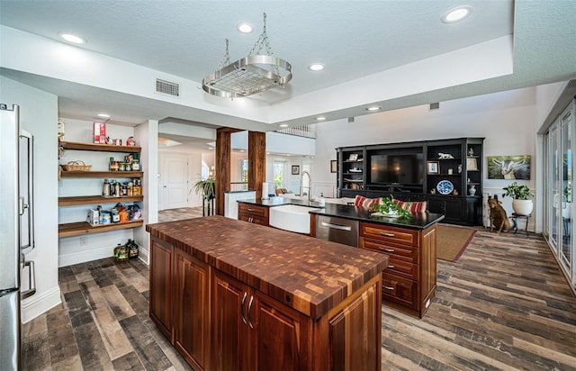 kitchen featuring dark wood-style floors, appliances with stainless steel finishes, a center island, wooden counters, and a sink