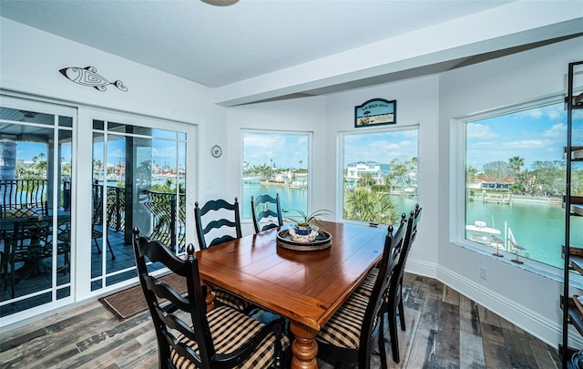 dining space with a water view, a textured ceiling, baseboards, and wood finished floors