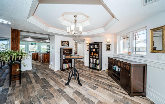 interior space with crown molding, a raised ceiling, visible vents, wood finished floors, and a chandelier