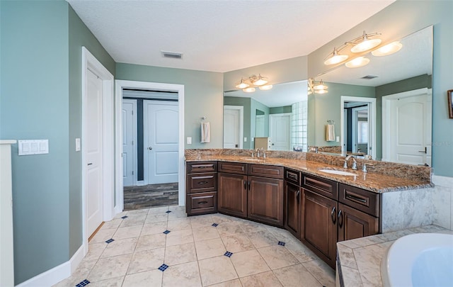 full bath featuring visible vents, a sink, a textured ceiling, and double vanity