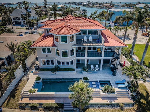 back of property with a patio, a balcony, a fenced backyard, a tile roof, and a water view