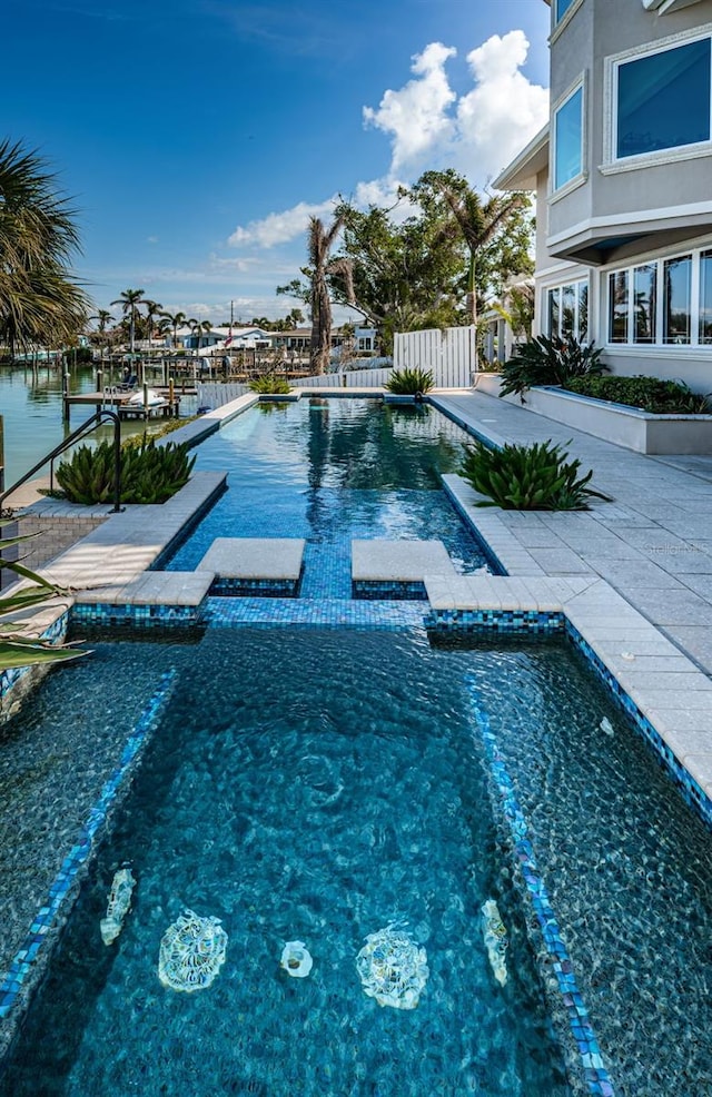 view of swimming pool featuring a water view, a patio area, a pool with connected hot tub, and fence