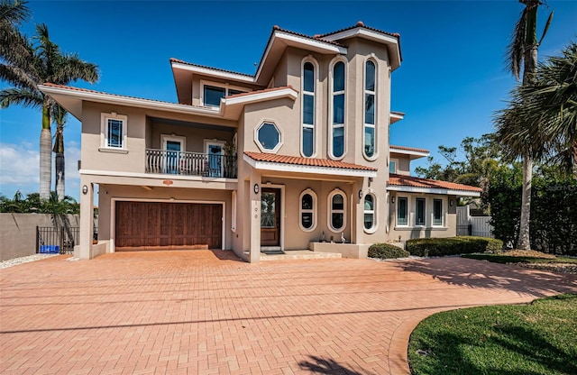 mediterranean / spanish house featuring a balcony, fence, decorative driveway, and stucco siding