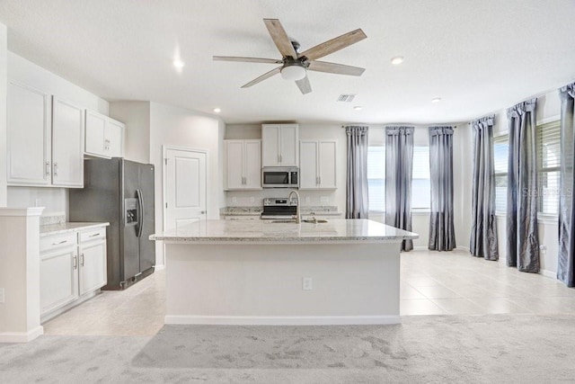 kitchen featuring white cabinetry, stainless steel appliances, light stone countertops, and a kitchen island with sink