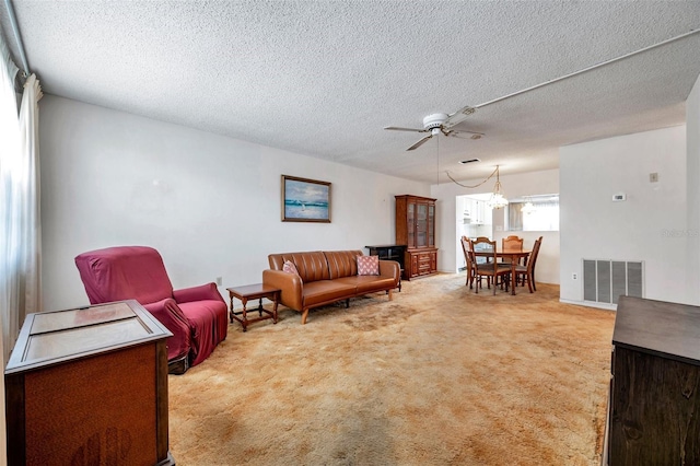 carpeted living room featuring ceiling fan with notable chandelier and a textured ceiling